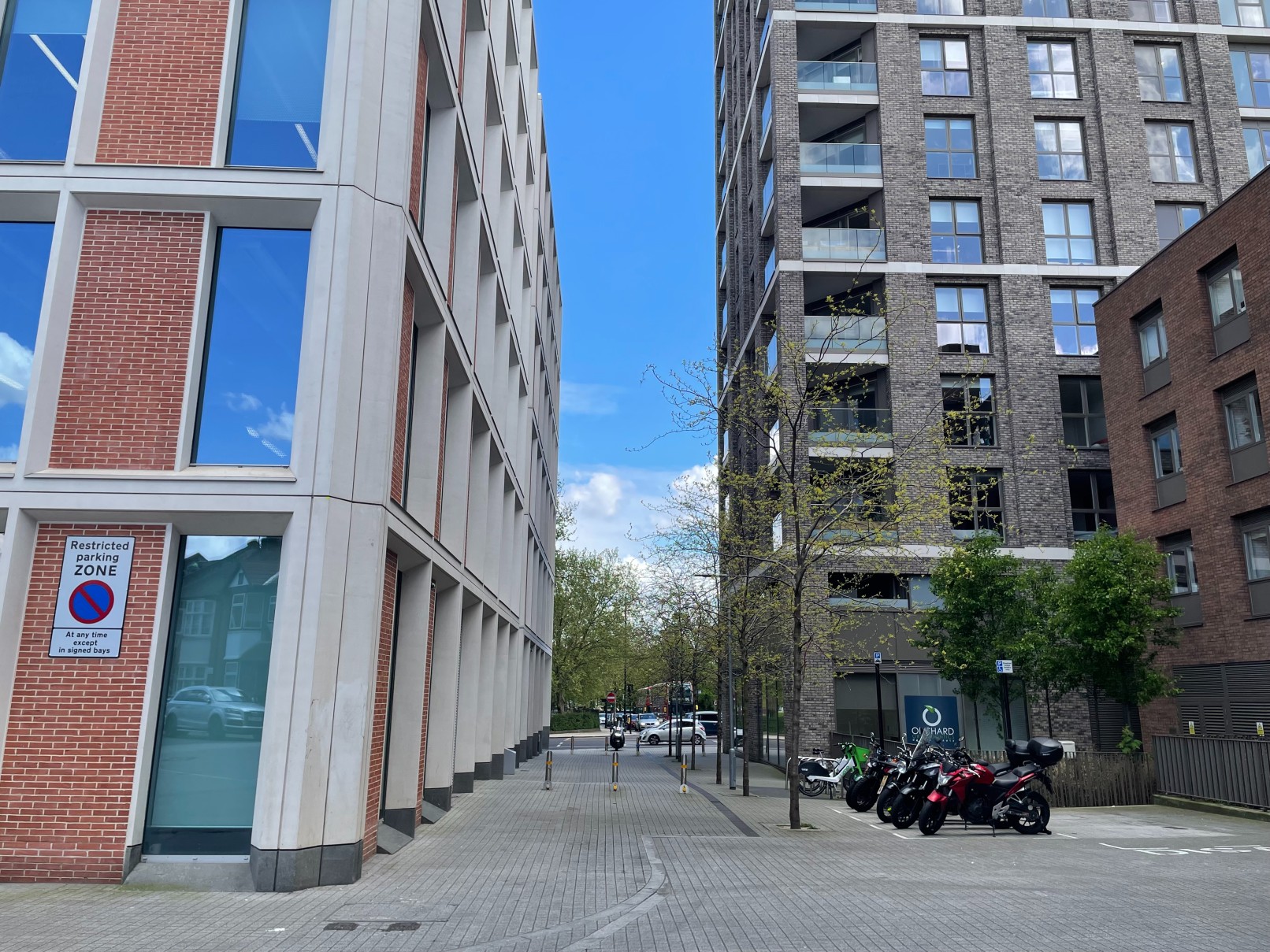 Modern buildings and parked motorcycles on a centre view of Porden Street, Lambeth, with a restricted parking zone sign.