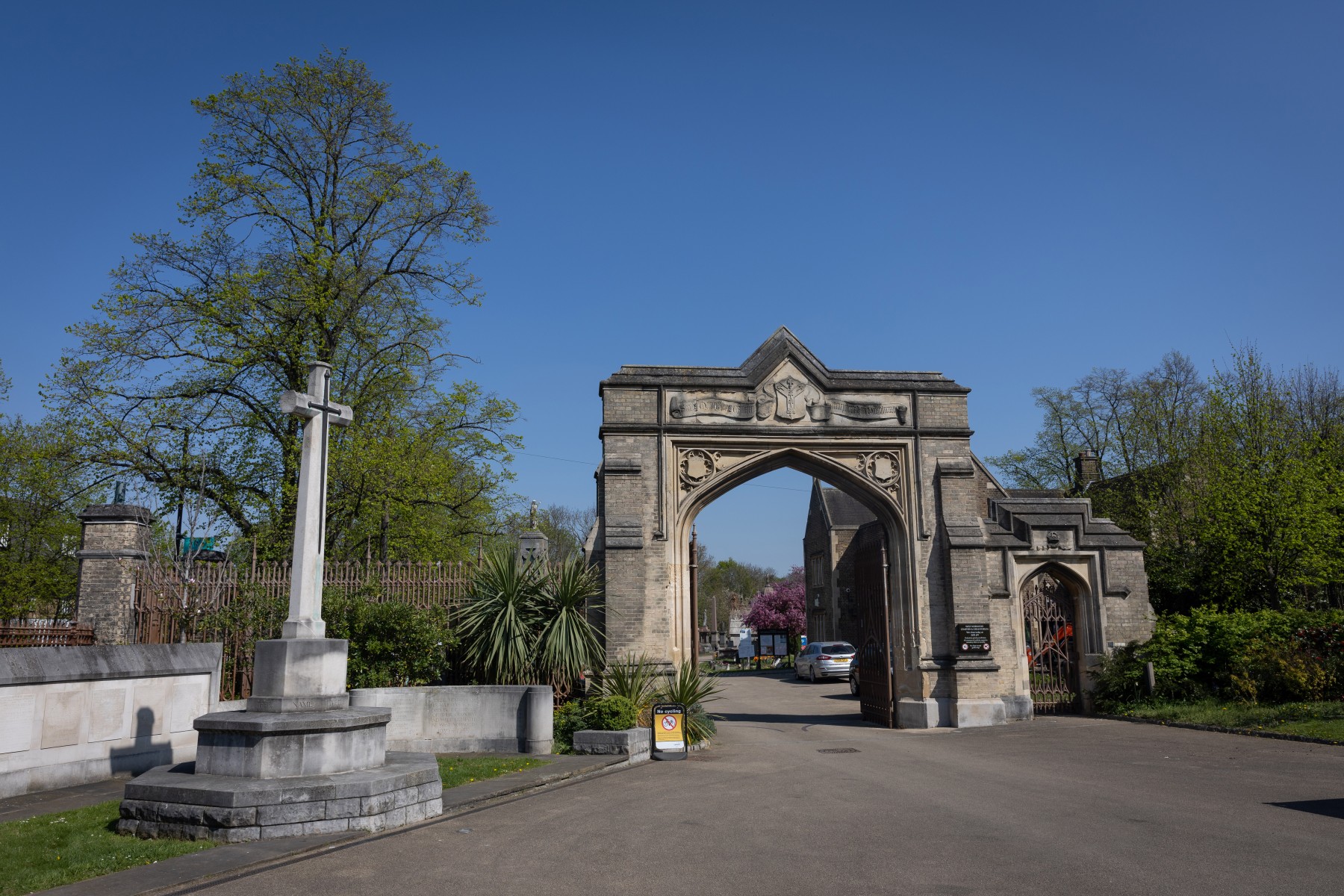 Entrance archway and memorial cross at West Norwood Cemetery under a clear blue sky.