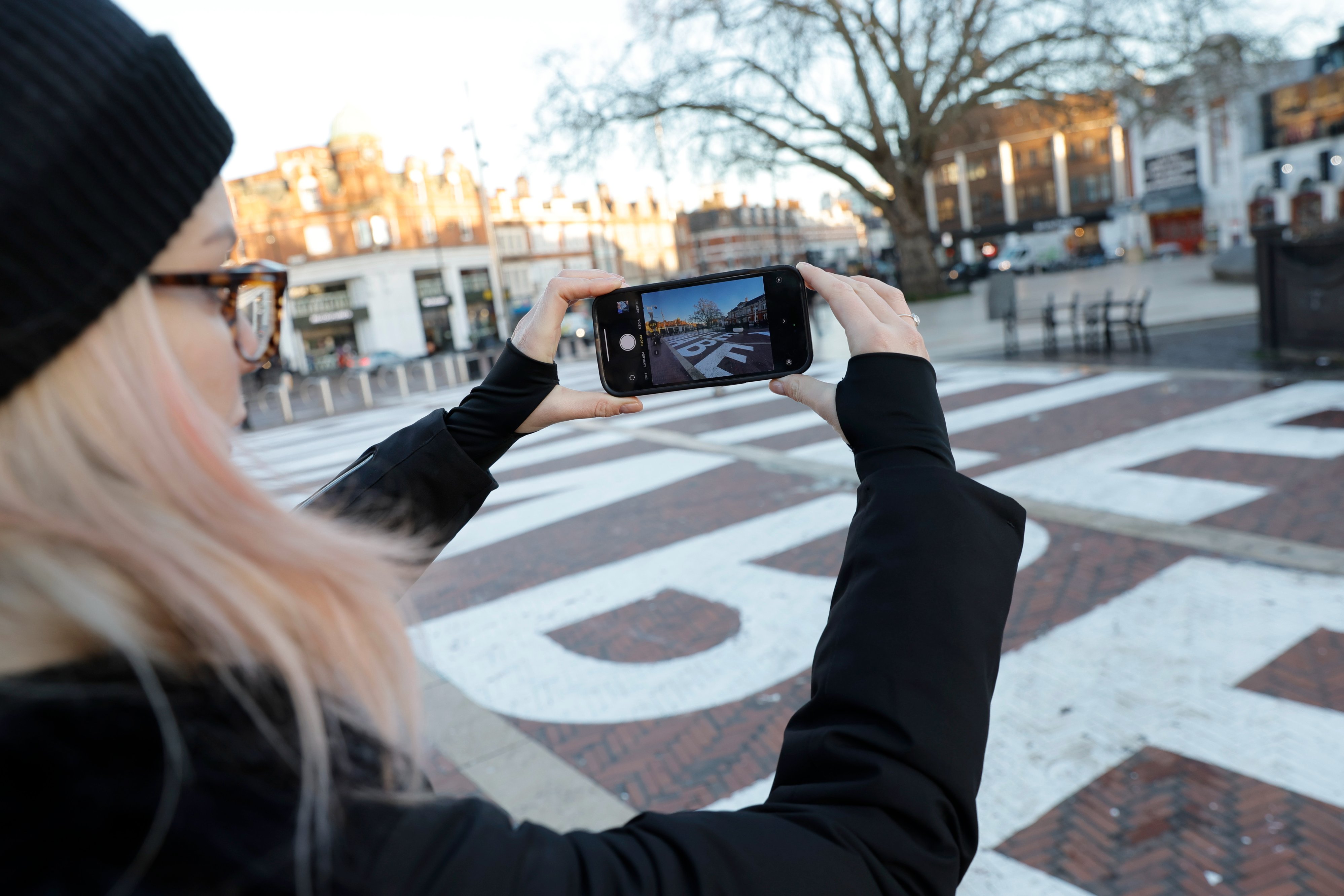 Woman taking a photo of the chalk mural artwork on the ground at Windrush Square