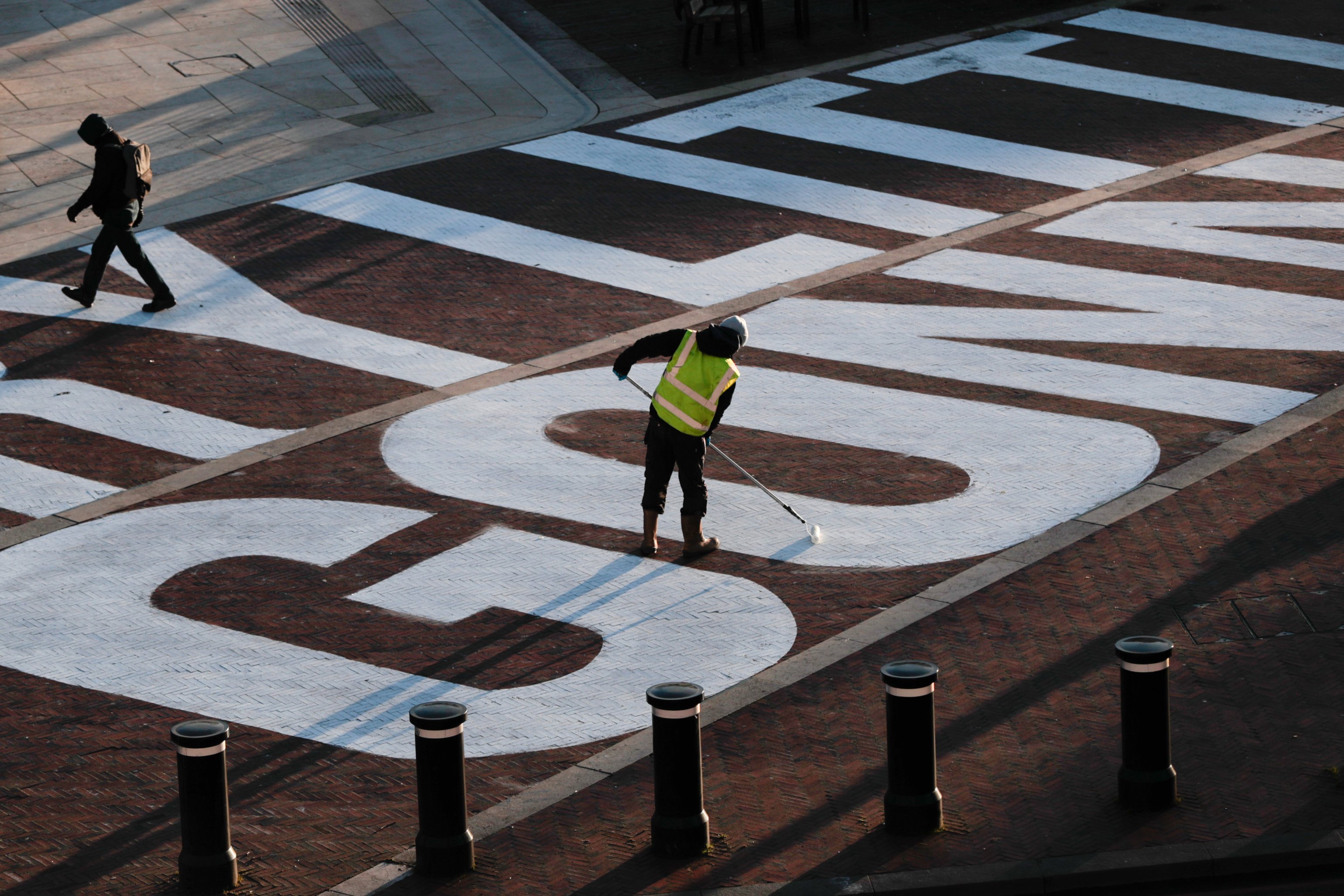 Man in high vis painting an 'O' in chalk onto the ground at Windrush Square