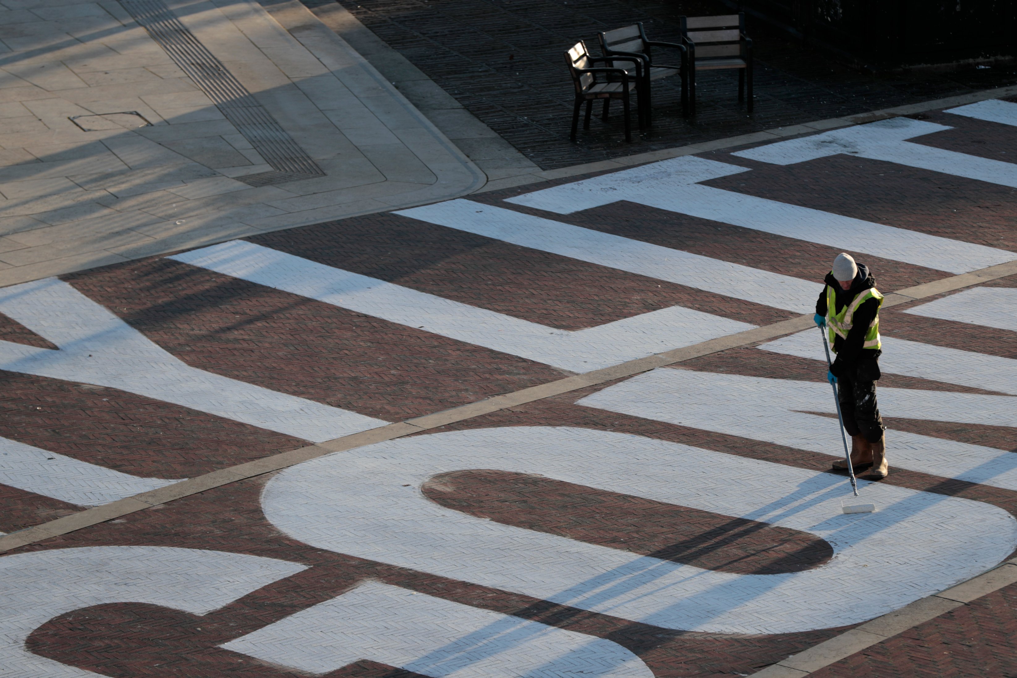 Man in high vis painting chalk mural onto the ground at Windrush Square